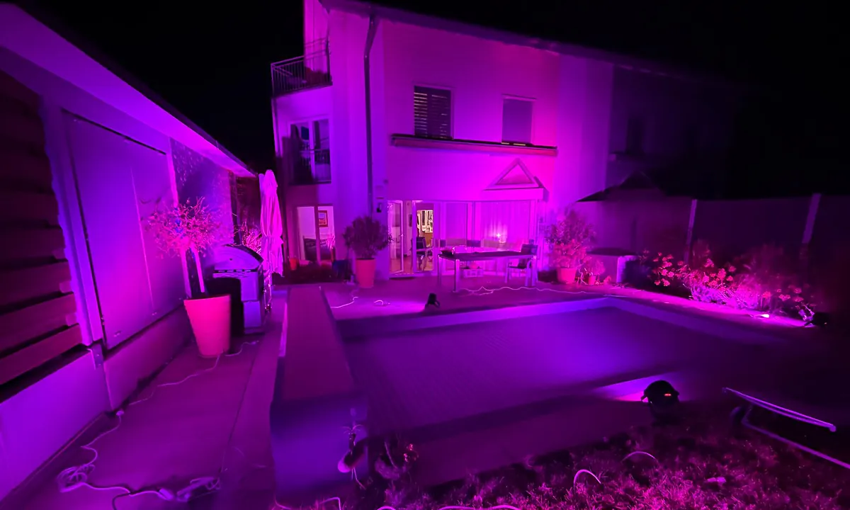 Garten mit Pool und Hausfassade in violettem und pinkem Licht