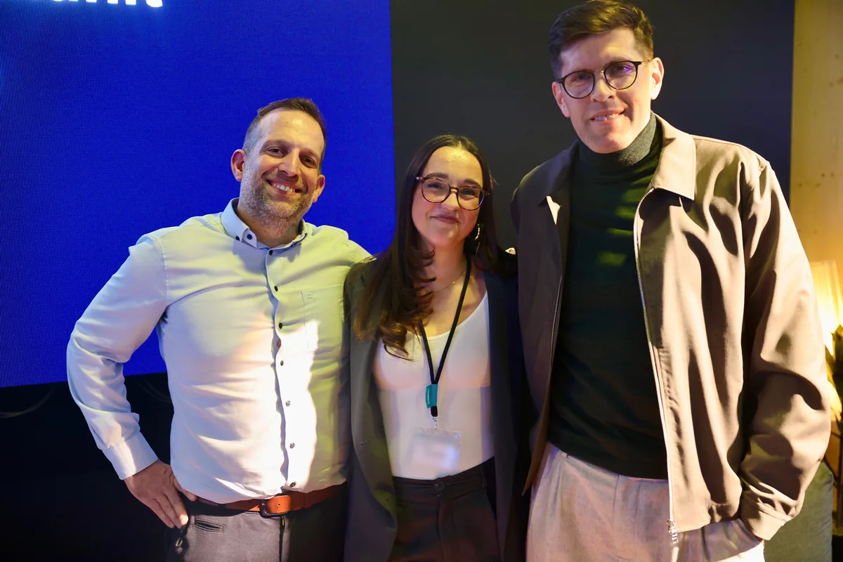 Drei Personen lächeln gemeinsam vor der blauen LED-Wand